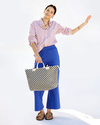 Aurelia holding the Black & Cream Checkers Le Zip Sac with a striped button down and cobalt la snap pants